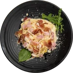 Spaghetti Spaghetti carbonara with ham and rocket on a black plate